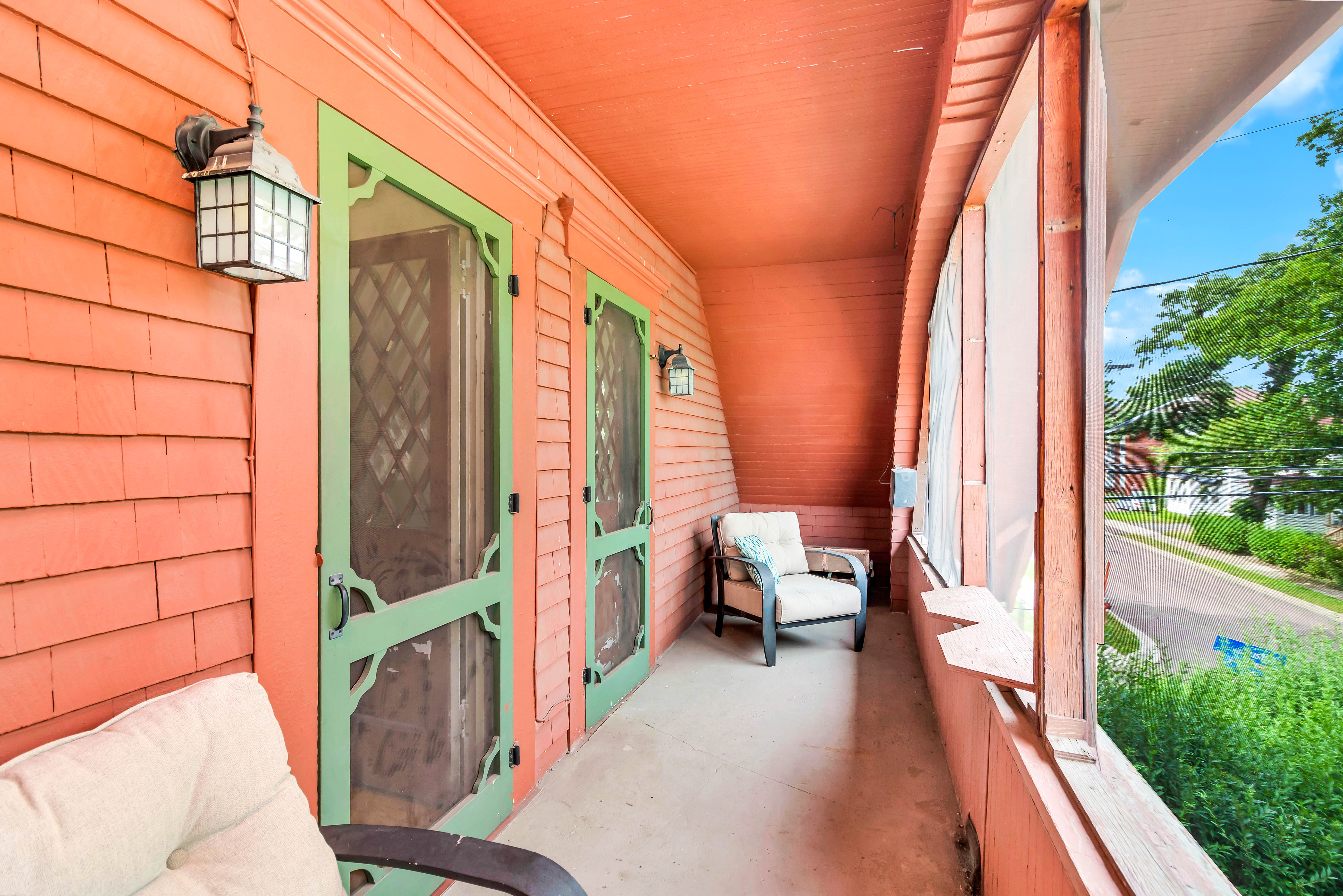 Upper screened-in balcony with coral siding, green trim doors, and cushioned seating—offering a relaxing street view retreat.