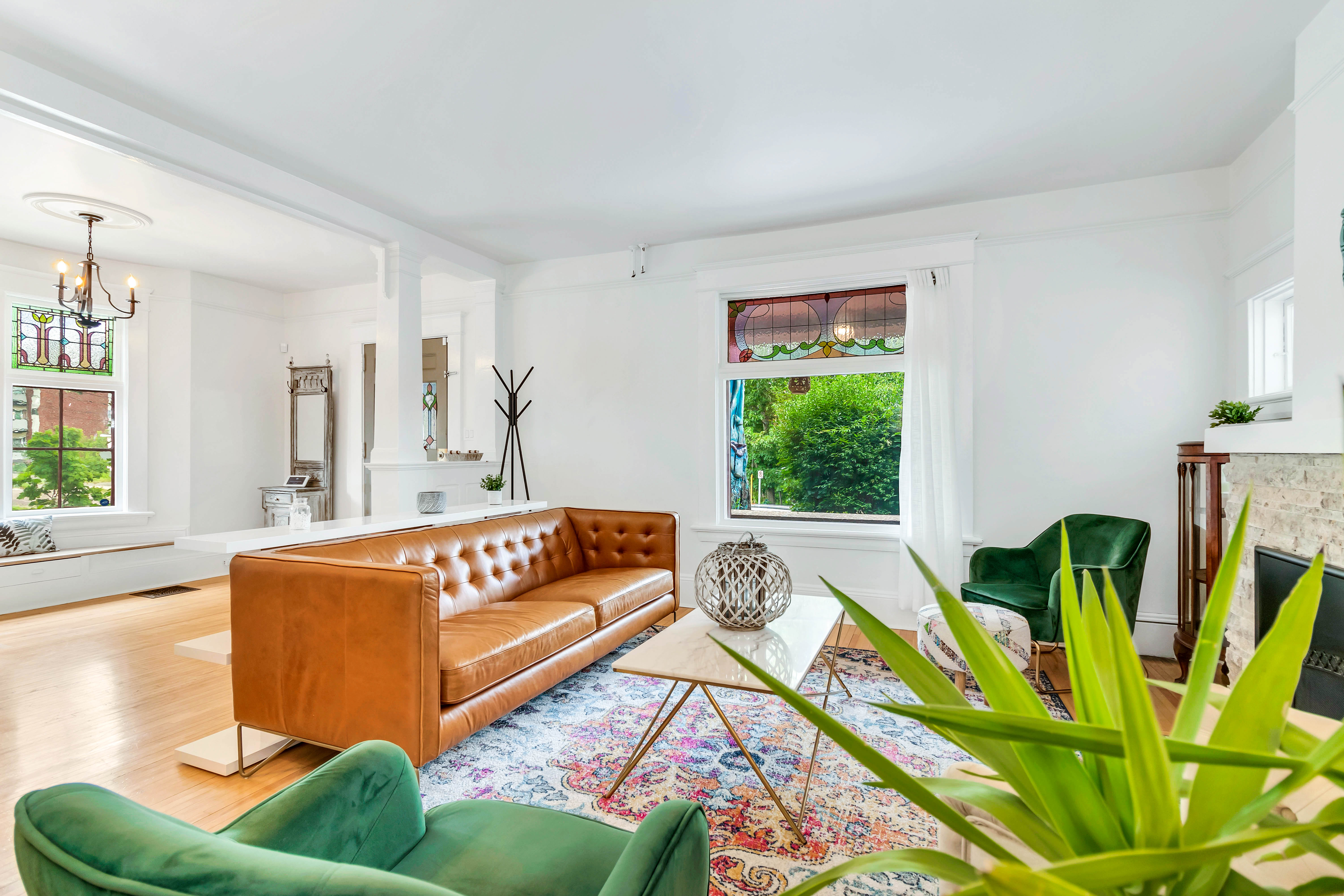 Spacious open-concept living area with a brown leather couch, large window with stained glass, and view of the entryway and staircase.