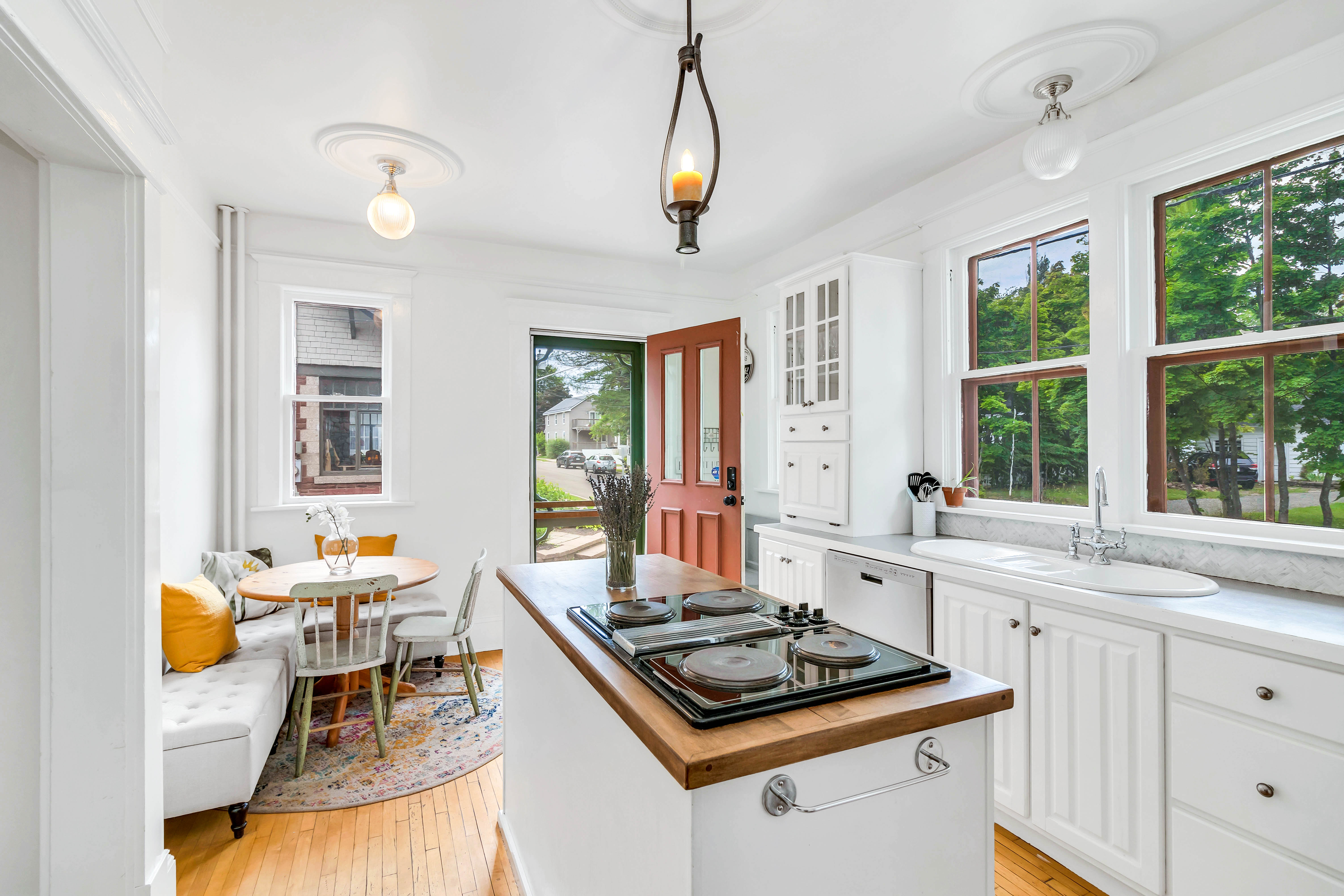 Charming kitchen nook featuring a cozy dining corner with banquette seating, round table, and colorful rug near side entrance with red door.