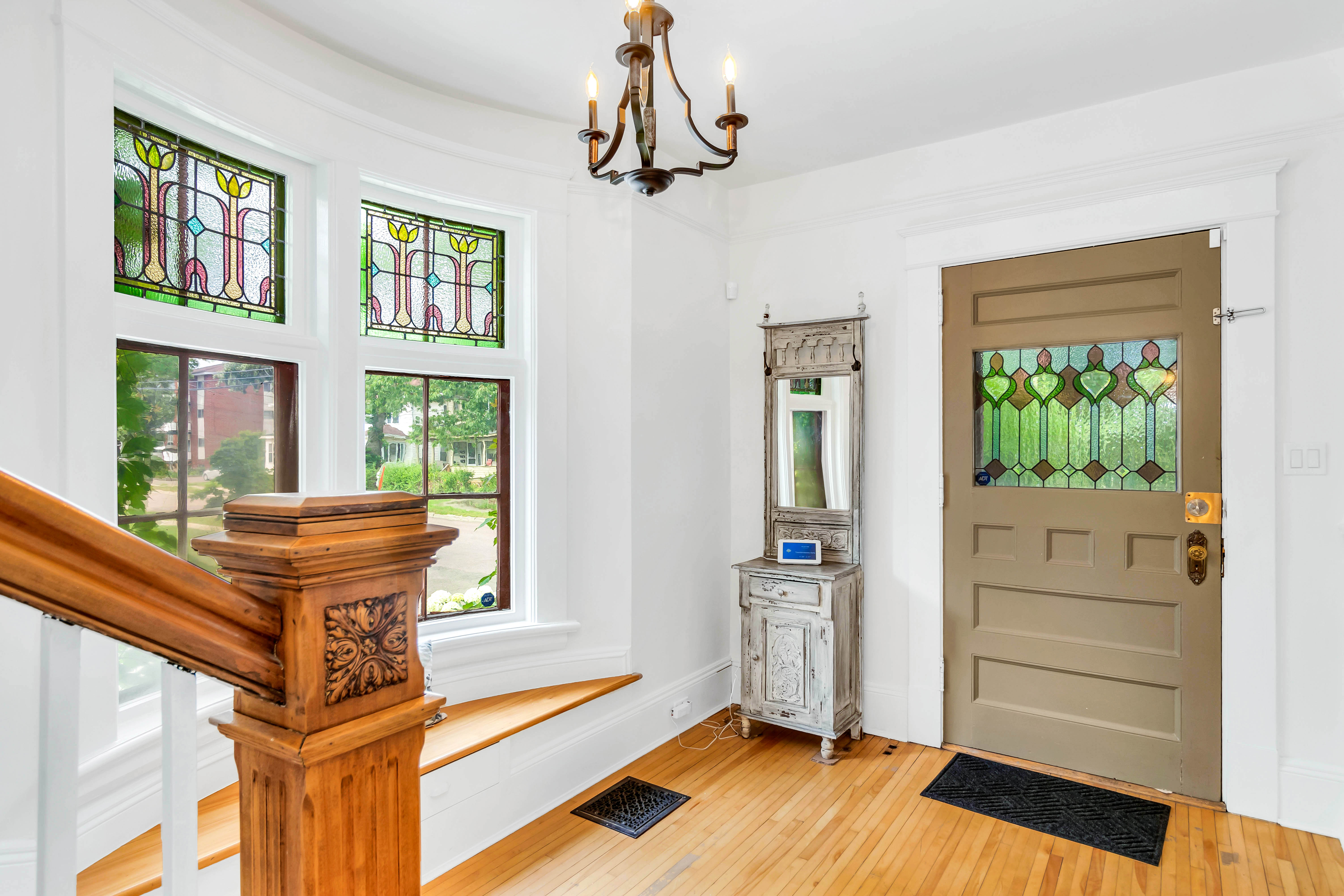Bright entryway with original hardwood floors, stained glass windows, a decorative chandelier, and vintage front door with colored glass panel.