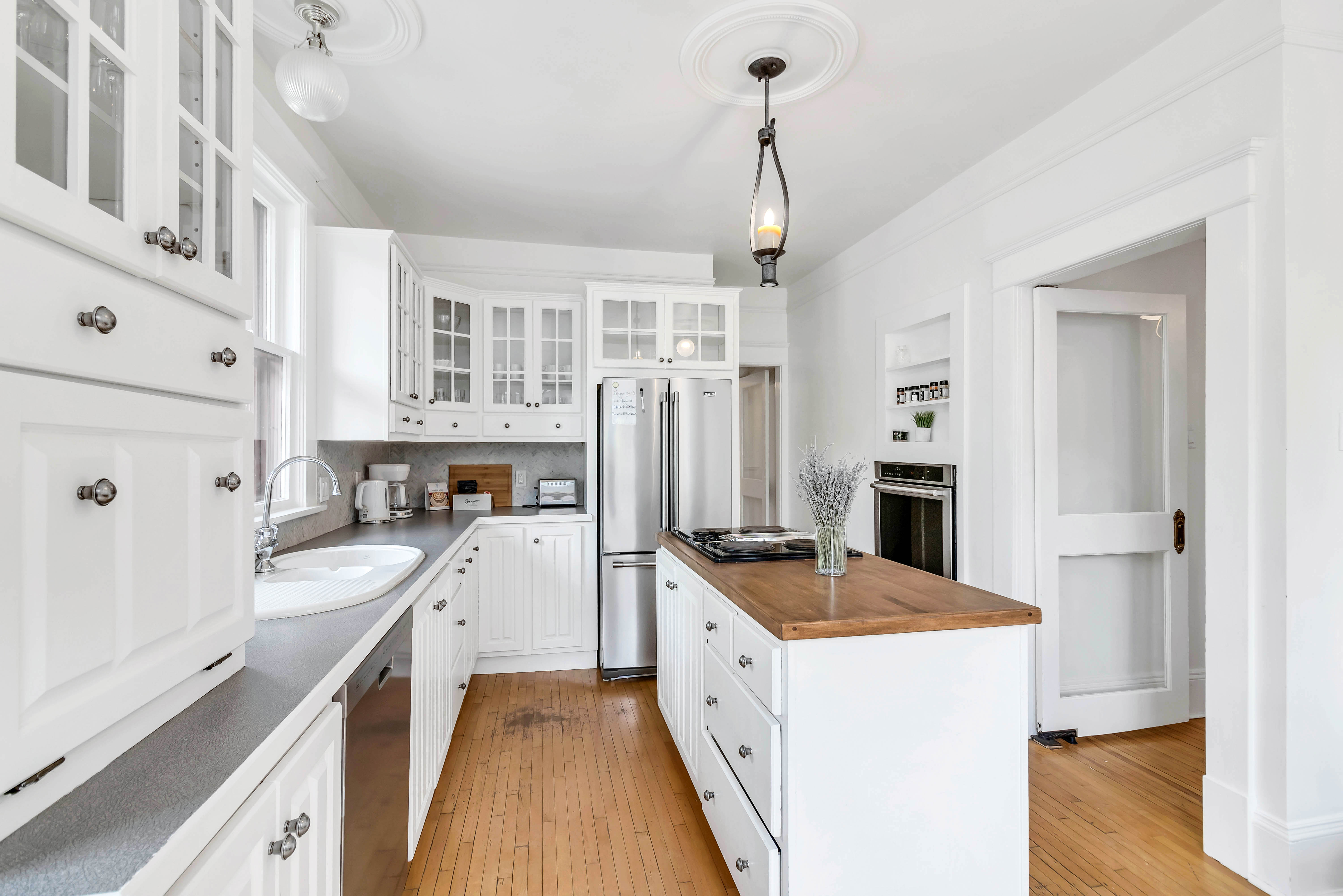 Bright white kitchen with shaker cabinets, stainless steel appliances, butcher block island, and pendant lighting. Classic charm meets modern function.