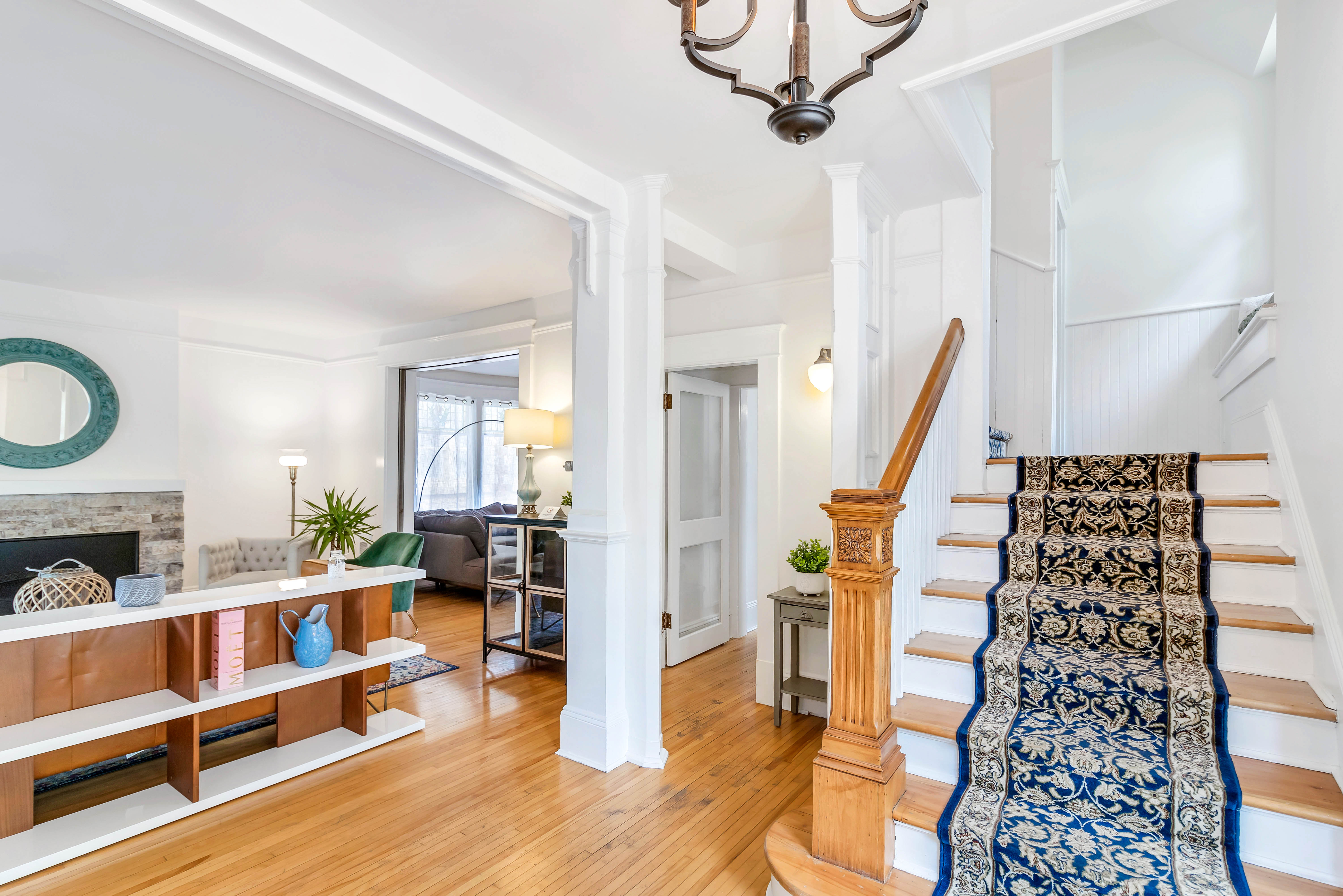 Elegant staircase with ornate wood detailing and a patterned runner, leading to upper floor, with open sightlines into living and sitting rooms.