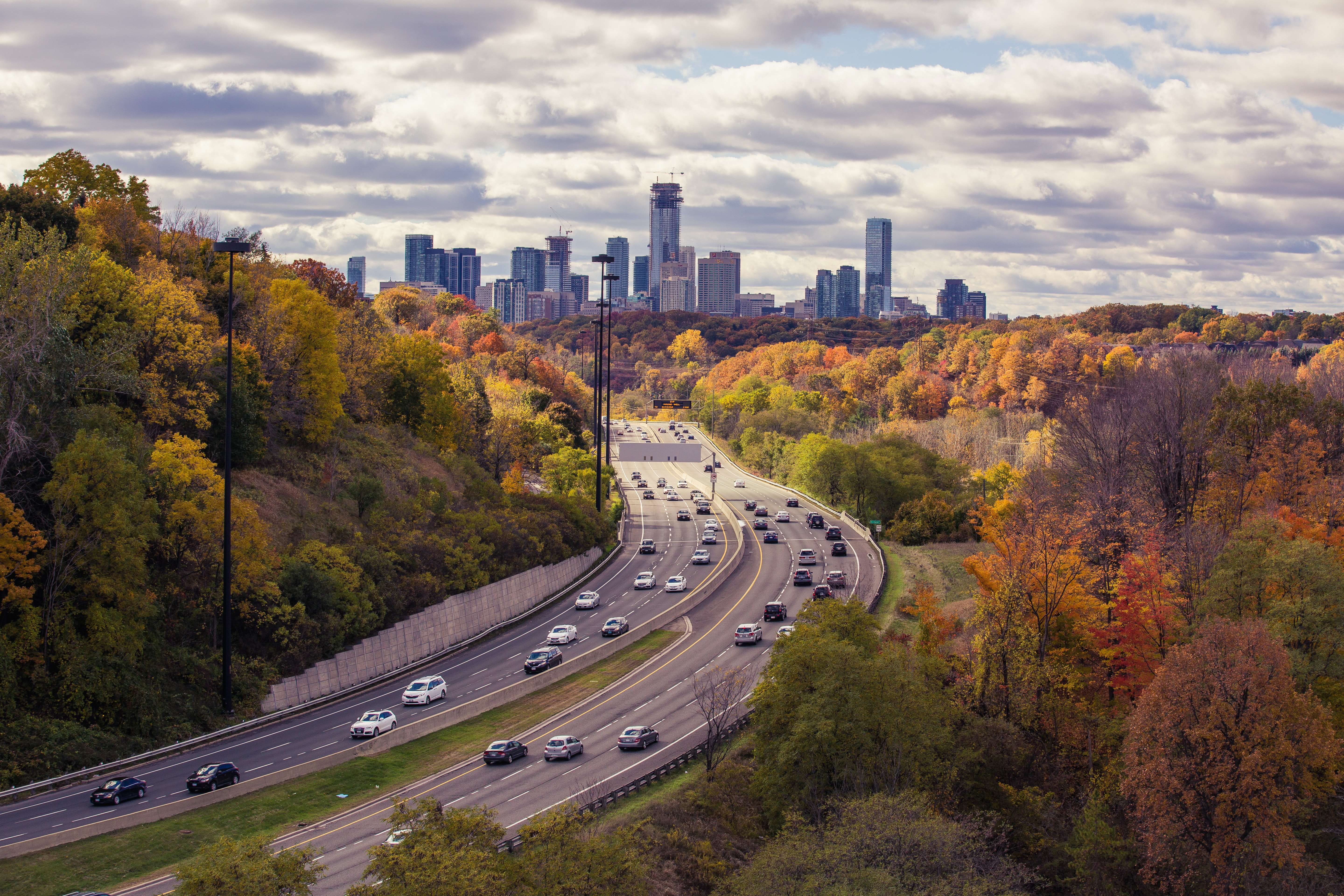 Aerial photo of a highway in Toronto with passing vehicles surrounded by autumn trees
