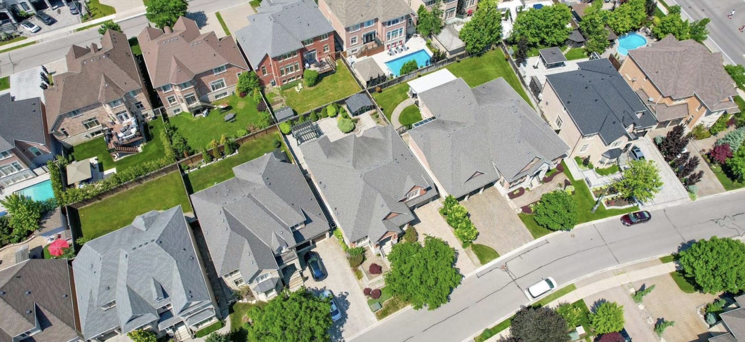 Overhead view of neighbouring detached homes with different rooflines, lots and backyards
